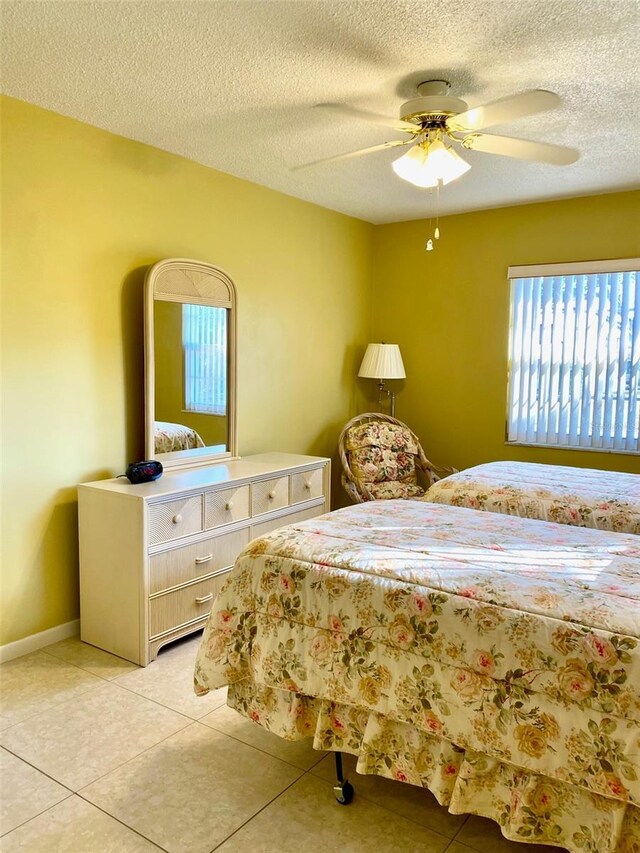 bedroom featuring light tile patterned floors, ceiling fan, a textured ceiling, and baseboards