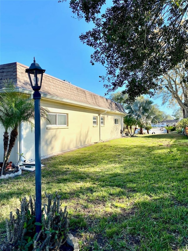 view of property exterior featuring stucco siding, mansard roof, and a yard