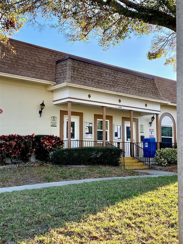 view of front facade featuring covered porch, mansard roof, a shingled roof, and stucco siding