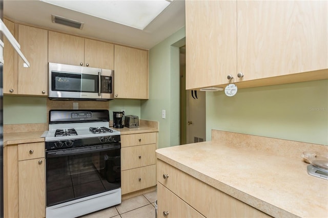 kitchen featuring visible vents, stainless steel microwave, light brown cabinets, and gas range