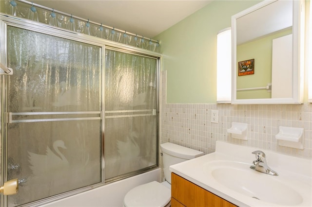 full bathroom featuring tile walls, combined bath / shower with glass door, vanity, and toilet