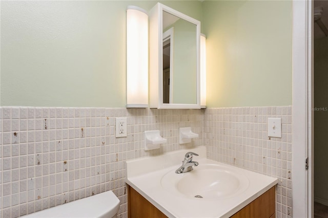 half bathroom with toilet, wainscoting, tile walls, and vanity