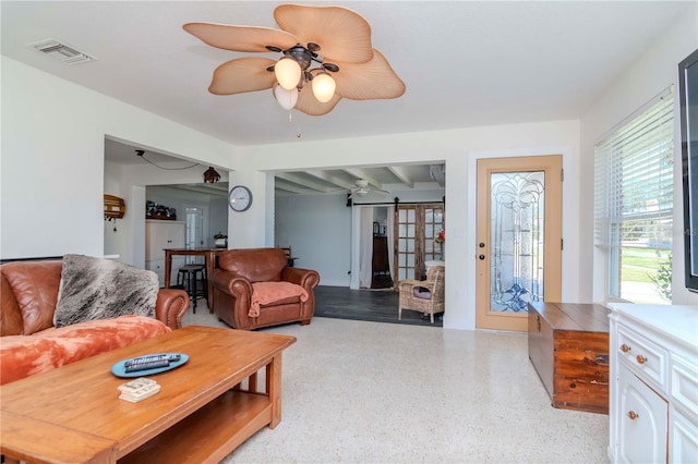 living area with ceiling fan, visible vents, and speckled floor