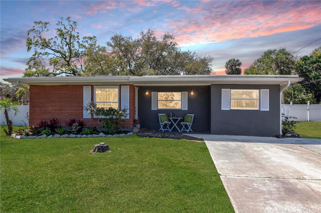 single story home featuring brick siding, fence, a front yard, stucco siding, and driveway