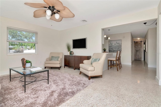living area featuring a ceiling fan, speckled floor, visible vents, a barn door, and baseboards