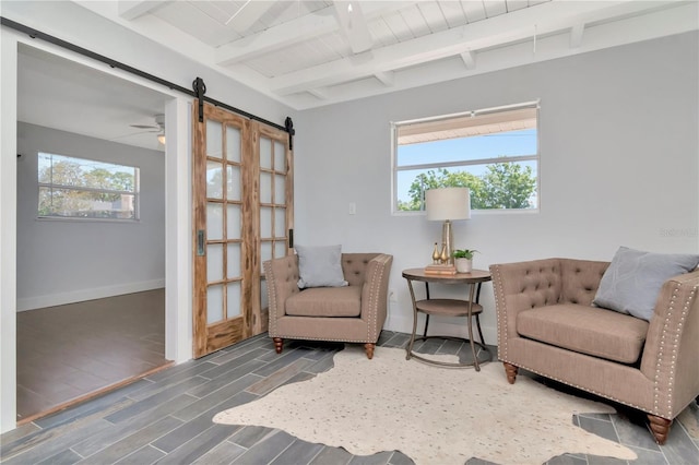 living area with baseboards, beamed ceiling, a barn door, and wood finished floors