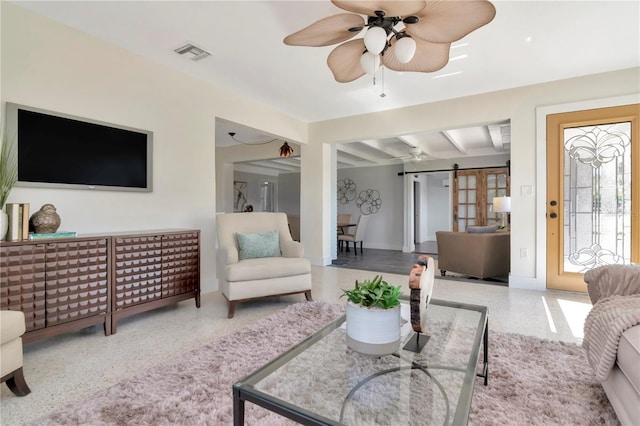 living room with a barn door, ceiling fan, visible vents, speckled floor, and beamed ceiling