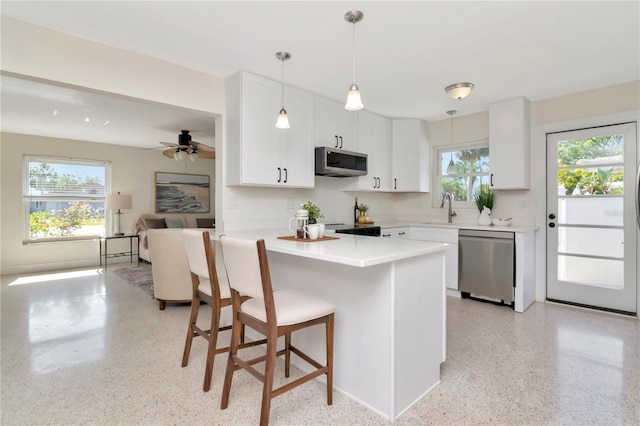 kitchen with a sink, stainless steel appliances, light speckled floor, white cabinetry, and a kitchen bar