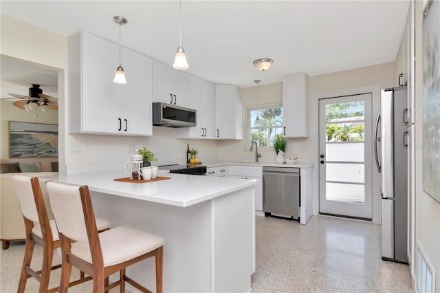 kitchen featuring a peninsula, a sink, a kitchen breakfast bar, appliances with stainless steel finishes, and light speckled floor