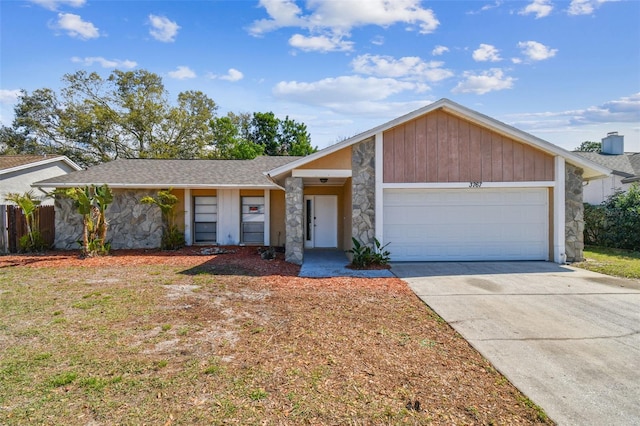 mid-century home with a garage, driveway, a shingled roof, stone siding, and fence