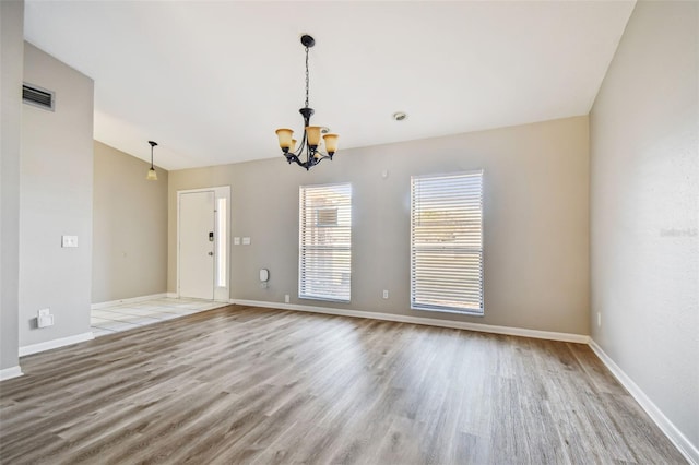 spare room with baseboards, visible vents, lofted ceiling, wood finished floors, and a notable chandelier