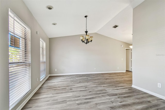 spare room featuring baseboards, visible vents, lofted ceiling, light wood-type flooring, and a notable chandelier