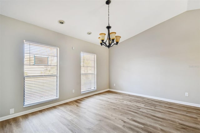 empty room featuring lofted ceiling, baseboards, a notable chandelier, and wood finished floors