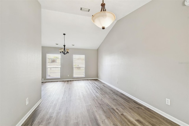 empty room with a chandelier, wood finished floors, visible vents, baseboards, and vaulted ceiling