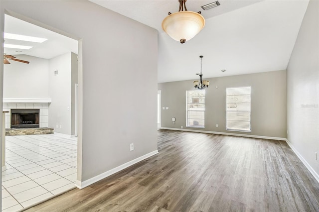 unfurnished room with baseboards, visible vents, a tiled fireplace, wood finished floors, and ceiling fan with notable chandelier