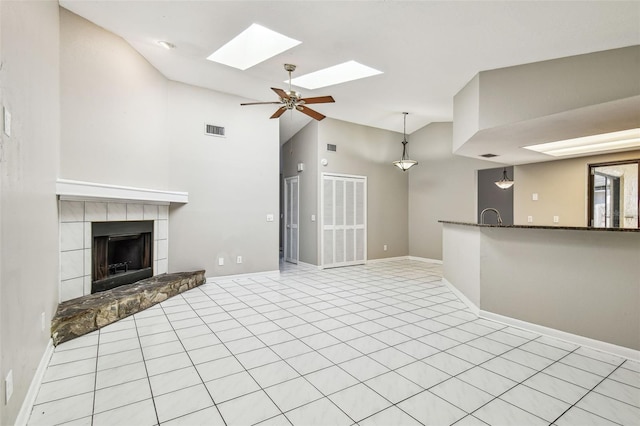 unfurnished living room with a tile fireplace, visible vents, vaulted ceiling with skylight, and baseboards