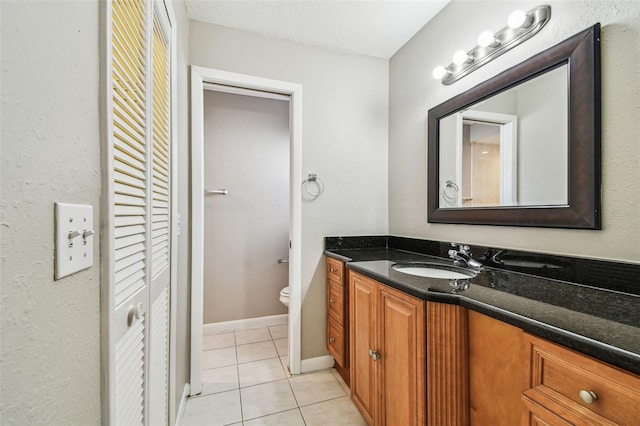 bathroom with a closet, toilet, vanity, baseboards, and tile patterned floors