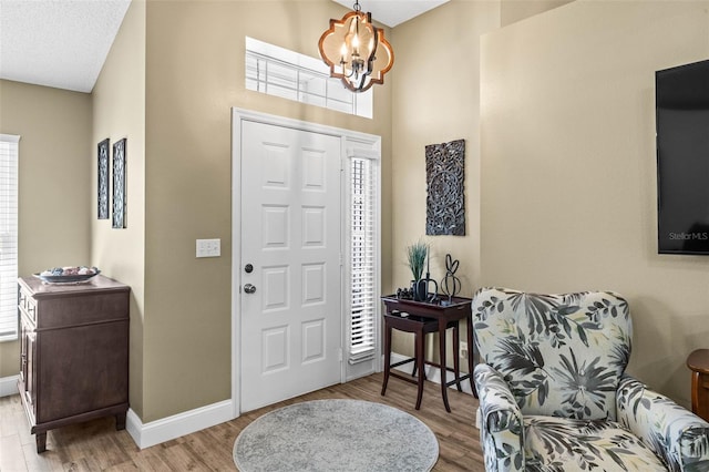 foyer featuring baseboards, light wood finished floors, a textured ceiling, and an inviting chandelier