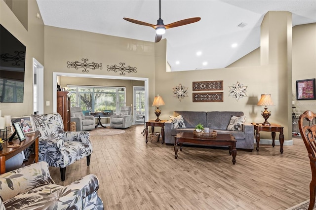 living room with ceiling fan, high vaulted ceiling, light wood finished floors, and visible vents