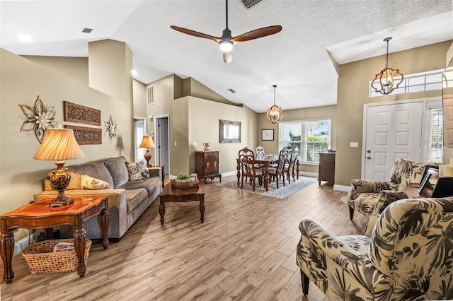 living area featuring visible vents, vaulted ceiling, a textured ceiling, light wood-style floors, and ceiling fan with notable chandelier