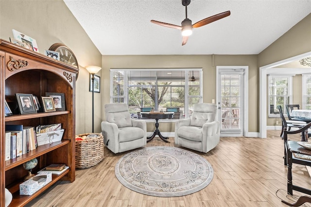 living area with lofted ceiling, ceiling fan, and light wood-style flooring