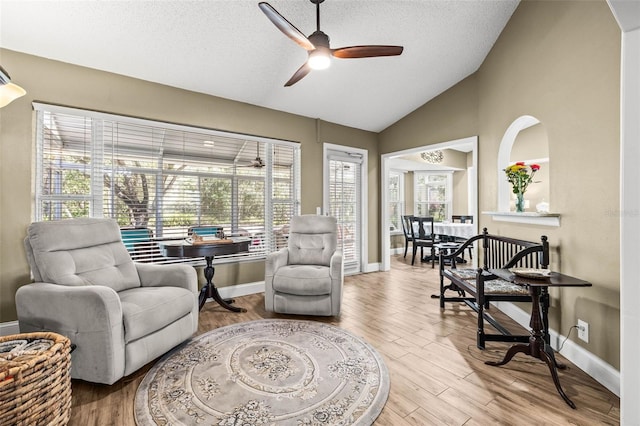 living area with baseboards, a ceiling fan, lofted ceiling, a textured ceiling, and light wood-style floors