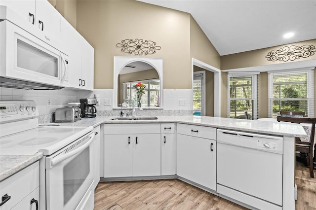 kitchen featuring white appliances, white cabinetry, a sink, and a peninsula