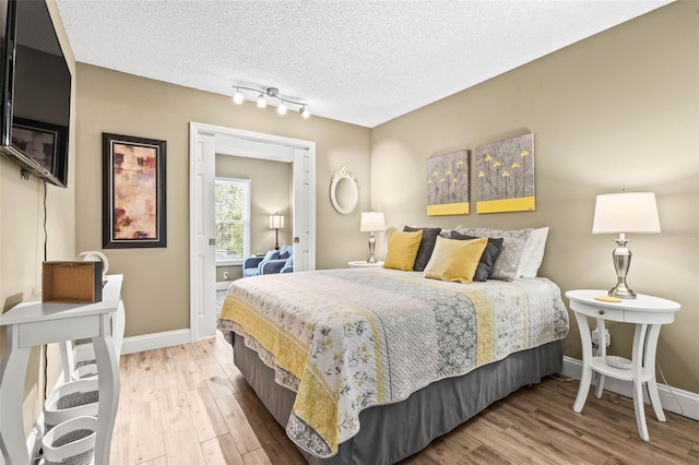 bedroom featuring rail lighting, a textured ceiling, baseboards, and wood finished floors