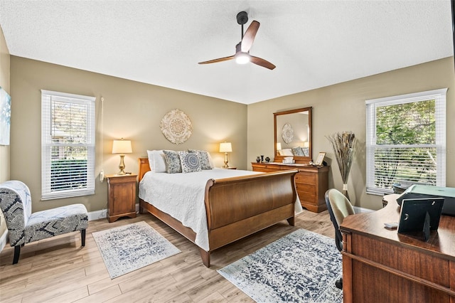 bedroom featuring light wood finished floors, ceiling fan, baseboards, and a textured ceiling