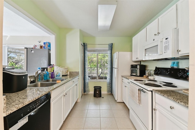 kitchen with light tile patterned floors, light stone counters, white appliances, a sink, and white cabinetry