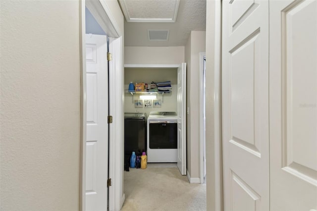 hallway featuring a textured ceiling, a textured wall, light carpet, visible vents, and washer and clothes dryer