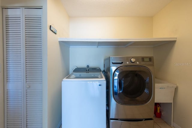 clothes washing area featuring laundry area, washer and clothes dryer, tile patterned floors, and baseboards