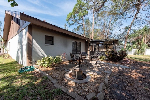 rear view of property featuring a fire pit, a patio, a sunroom, and stucco siding