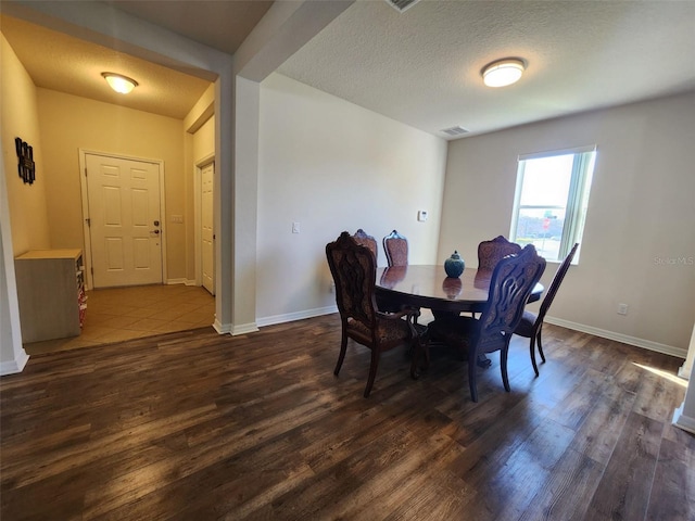 dining space featuring baseboards, a textured ceiling, visible vents, and dark wood-style flooring