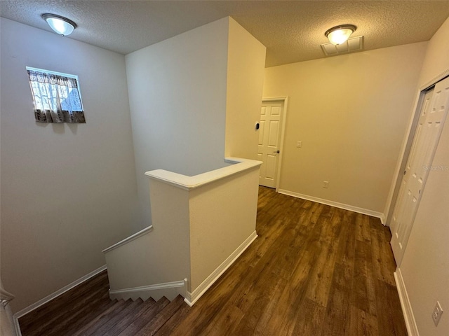 hall featuring dark wood-style floors, a textured ceiling, an upstairs landing, and baseboards