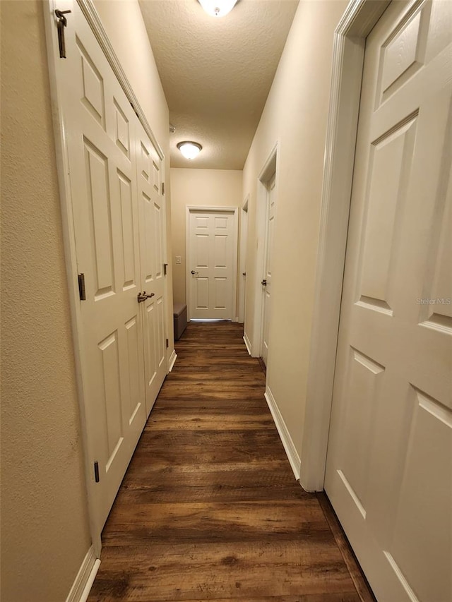 hallway featuring dark wood-style floors, a textured ceiling, and baseboards