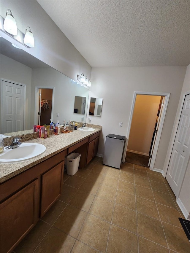 bathroom with double vanity, a sink, a textured ceiling, and tile patterned floors