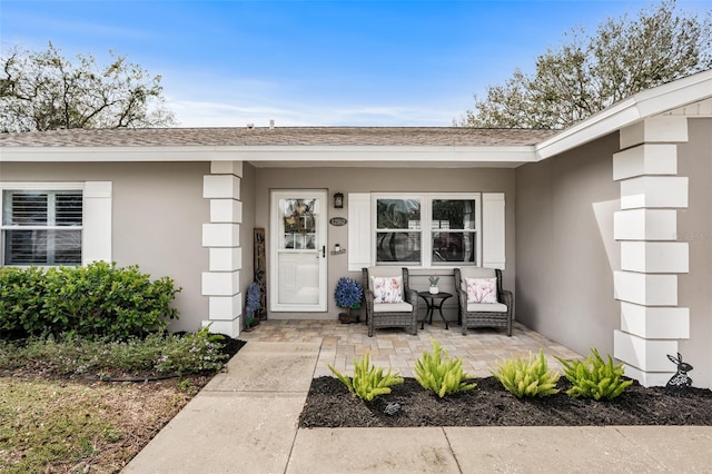 entrance to property featuring a shingled roof and stucco siding