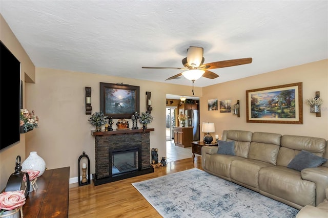 living area with baseboards, ceiling fan, a textured ceiling, light wood-style floors, and a fireplace