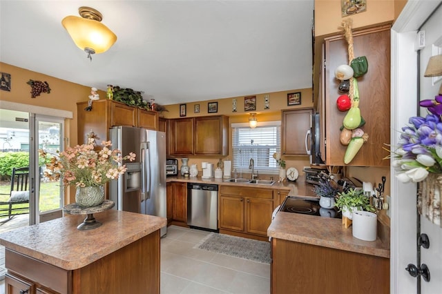 kitchen featuring light tile patterned floors, appliances with stainless steel finishes, brown cabinetry, and a sink