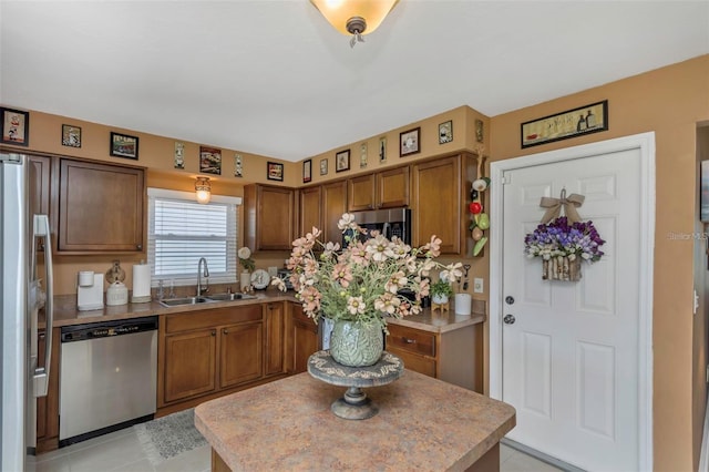 kitchen featuring light tile patterned flooring, stainless steel appliances, a sink, light countertops, and brown cabinetry