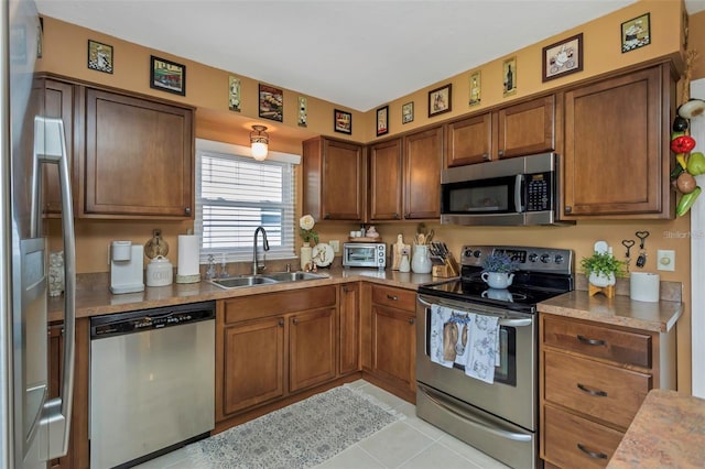 kitchen featuring stainless steel appliances, brown cabinets, light countertops, and a sink