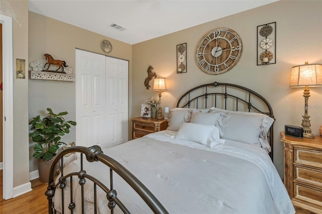 bedroom with light wood-type flooring, baseboards, visible vents, and a closet