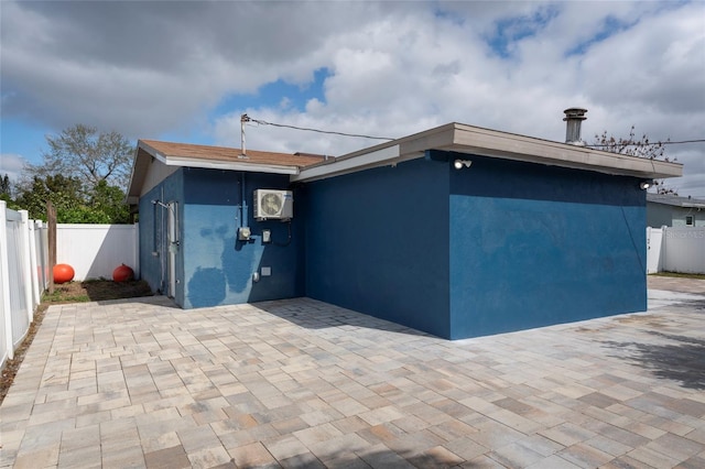 exterior space featuring an AC wall unit, a patio area, fence, and stucco siding