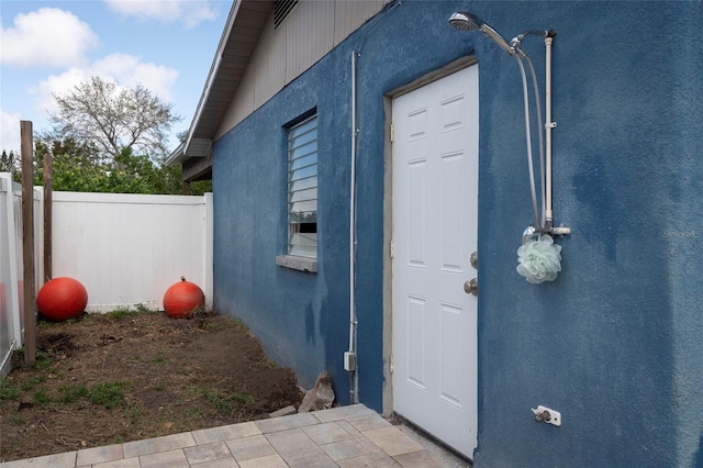 doorway to property featuring fence and stucco siding