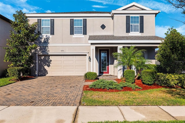 traditional-style home featuring an attached garage, decorative driveway, and stucco siding