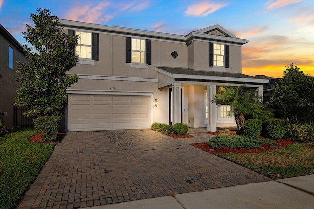 traditional-style home featuring decorative driveway, an attached garage, and stucco siding