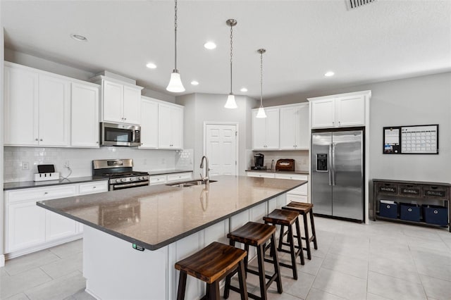 kitchen with stainless steel appliances, a sink, white cabinetry, backsplash, and a kitchen bar