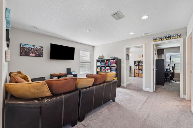 living area with a healthy amount of sunlight, visible vents, a textured ceiling, and light colored carpet