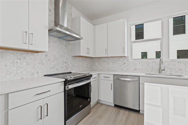 kitchen with appliances with stainless steel finishes, light countertops, a sink, and wall chimney range hood